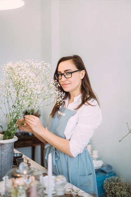 Small business. Florist girl is focused in a flower shop. Bright studio of floral design, decor. Flower delivery, order creation