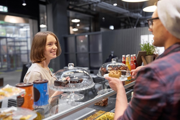 small business, food, people and service concept - happy man or barman with cake serving female customer at vegan cafe