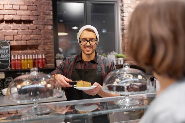 small business, food, people and service concept - happy man or barman with cake serving female customer at vegan cafe