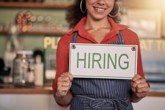 カフェやコーヒーショップで求人募集のサインを持つ中小企業の手や黒人女性、求人マーケティングや幸せな起業家が店頭でオンボレーディングメッセージを浮かべて微笑む