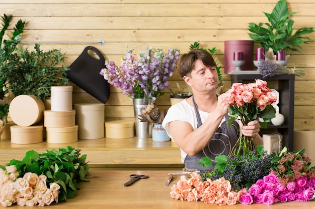 Small business. Male florist making rose bouquet at counter desk in flower shop. Man assistant or owner in floral shop, making decorations and arrangements. Flowers delivery, creating order