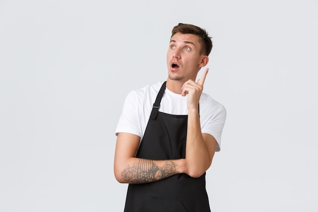 Small business owners, coffee shop and staff concept. Creative handsome barista having an idea, looking upper left corner gasping astounded and raise index finger, give suggestion, think-up plan