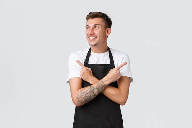 Small business owners, coffee shop and staff concept. Excited handsome smiling barista, waiter in cafe pointing fingers sideways and looking left happy, making choice, have variants, white background