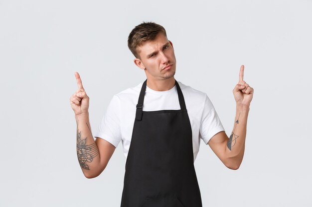 Small business owners, coffee shop and staff concept. Skeptical and dispelased barista in black apron judging, looking disapponted and annoyed, pointing fingers up and scolding someone