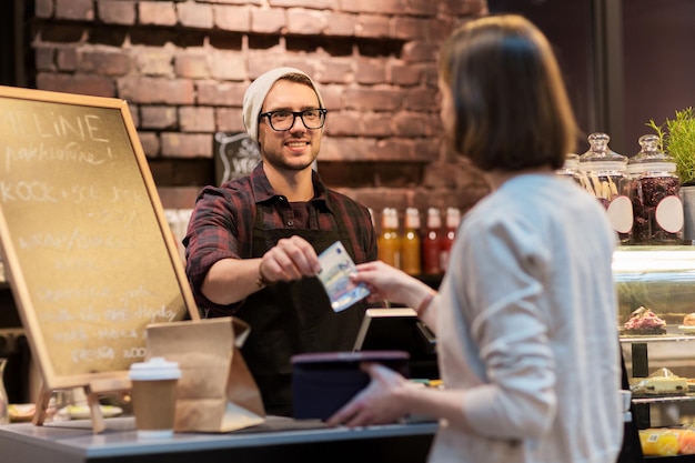 small business, payment, people and service concept - happy barman and woman paying money at cafe