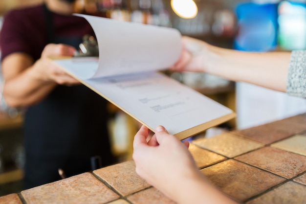 Photo small business, people and service concept - bartender showing menu to customer at bar or coffee shop