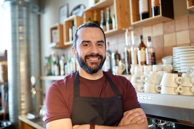 small business, people and service concept - happy man or waiter in apron at bar or coffee shop