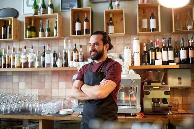 small business, people and service concept - happy man or waiter in apron at bar or coffee shop