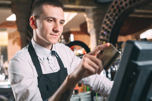 Малый бизнес, люди и концепция обслуживания - счастливый человек или официант в фартук на прилавке с кассы работает в баре или кафе