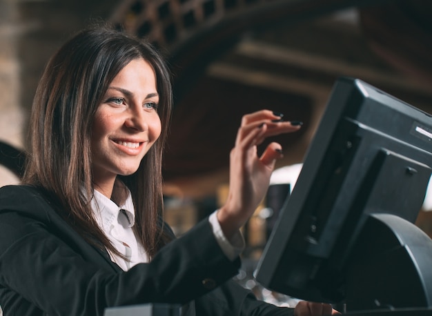 Small business, people and service concept - happy woman or waiter or manager in apron at counter with cashbox working at bar or coffee shop