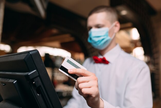 Small business, people and service concept. man or waiter in medical mask at counter with cashbox working at bar or coffee shop.