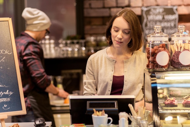 中小企業、人々、サービスのコンセプト – キャッシュボックスを備えたカフェまたはコーヒーショップのカウンターにいる女性またはバーテンダー