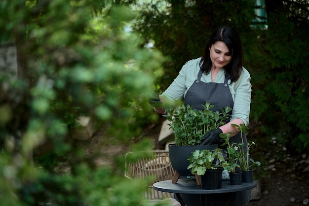 Small business Woman in an apron and mittens plants flowers in a wooden pot on a background of green garden