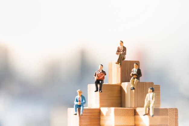 Small businessmen figures sitting on wooden blocks step with city backgrounds.