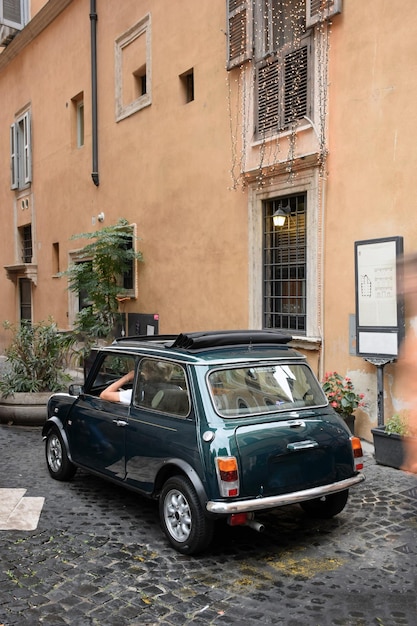 A small car with a driver near the wall of an old house with\
flower pots