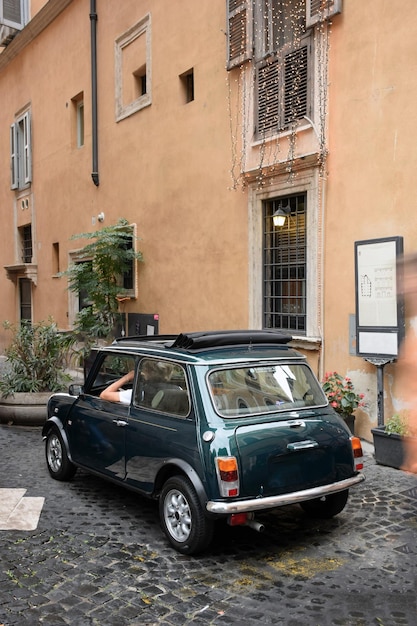 Foto una piccola macchina con autista vicino al muro di una vecchia casa con vasi di fiori