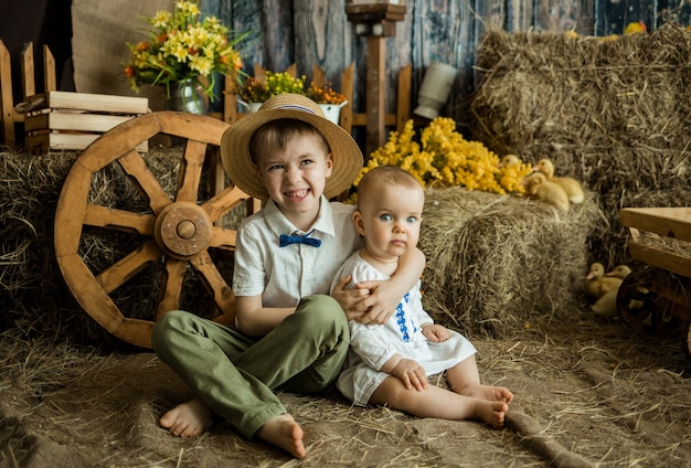 Small Caucasian brother and sister sit on straw in an Easter decoration with a haystack and ducklings. Easter for children