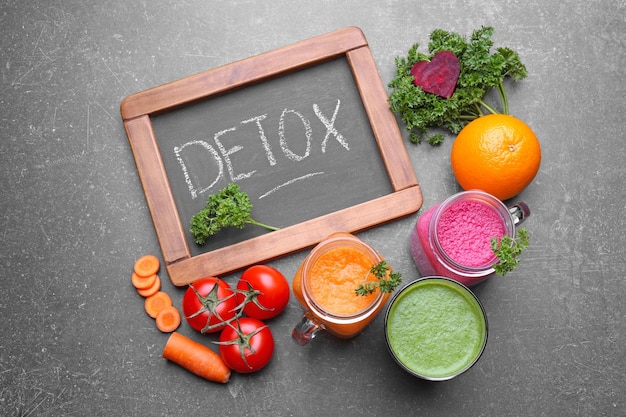 Small chalkboard with word DETOX vegetable juices and ingredients on table
