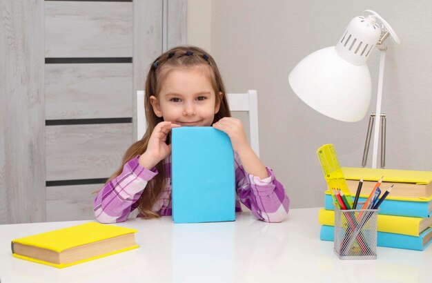 Small, charming girl holds a book in her hands. does school homework at home. Selective focus.