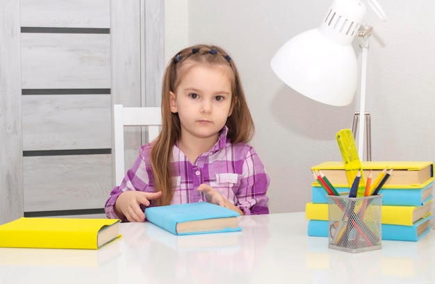 Small, charming girl is sitting at table with books, preparing for school.Selective focus.