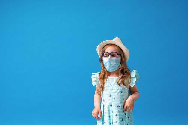 Small cheerful girl in glasses, hat, and summer dress poses