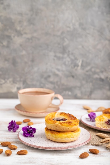 Small cheesecakes with jam and almonds with cup of coffee on a white wooden background Side view copy space