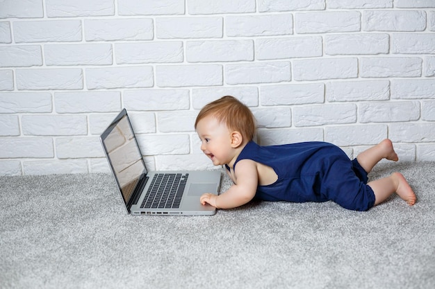 A small child 67 months old in a blue cotton overalls sits with an open laptop and watches educational games