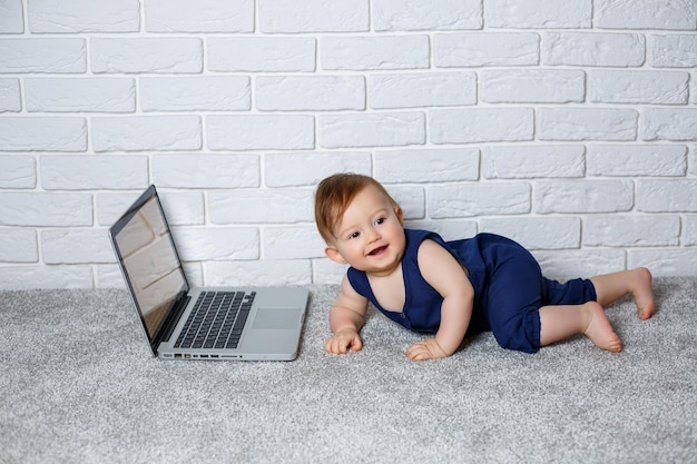 파란색 면 작업복을 입은 67개월 된 작은 아이가 열린 노트북과 함께 앉아 교육 게임을 시청합니다