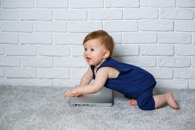 A small child 67 months old in a blue cotton overalls sits with an open laptop and watches educational games