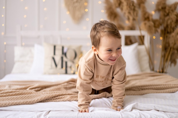 A small child on a bed in beige brown natural tones is laughing and rejoicing a cheerful and funny little kid is playing at home