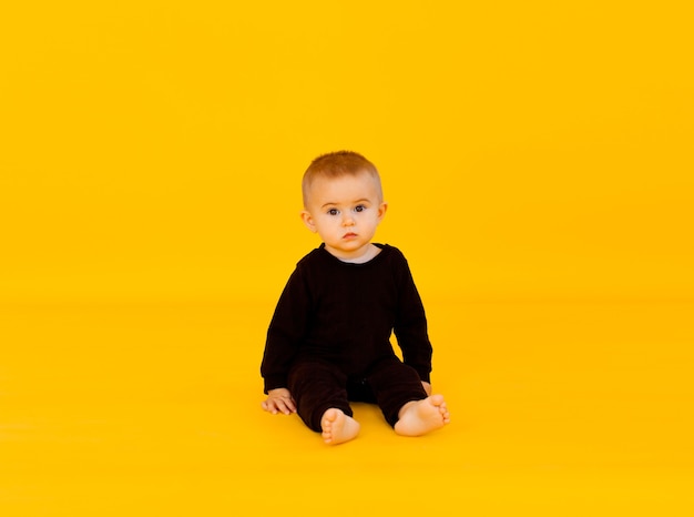 黒のボディースーツを着た小さな子供。彼は黄色いスタジオの背景に微笑んでいます。子供の頃、赤ちゃんの広告に関する記事。スペースをコピーし、クローズアップ