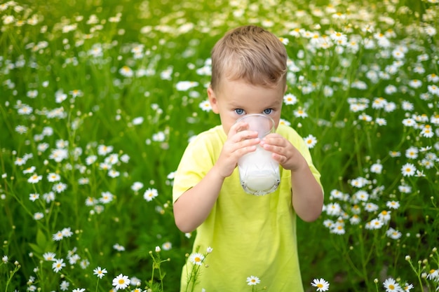 A small child a boy in clothes made of natural cotton walks\
around the field holds a glass of milk in his hands enjoys life\
enjoys nature