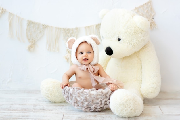 A small child a boy is sitting in a basket in a bear hat with a large Teddy bear.