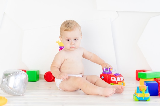 A small child a boy six months old plays with bright toys in a bright white room in diapers