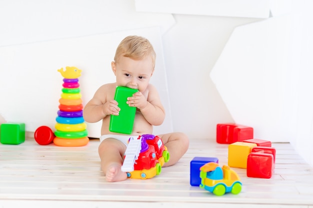 A small child a boy of six months plays with bright toys in a bright white room in diapers and nibbles them