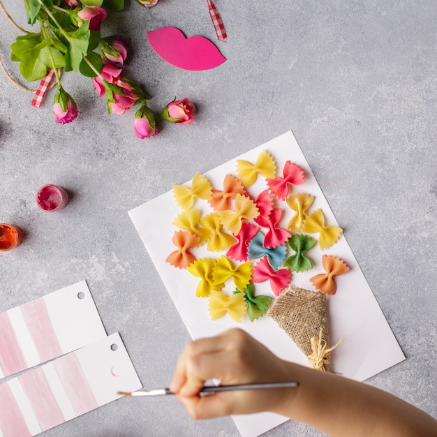 Small child doing a bouquet of flowers out of colored paper and colored pasta.