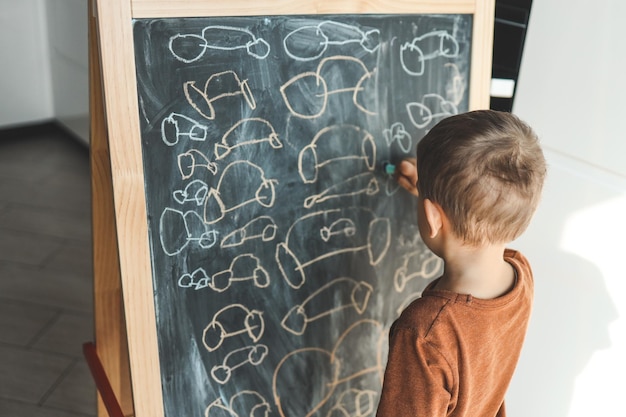 A small child draws a chalk on an easel