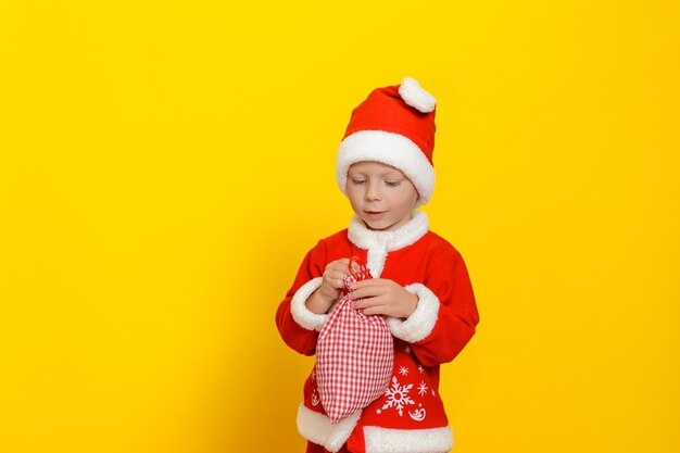 A small child dressed in a red santa claus costume is holding a small sack with new years gifts