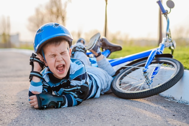 小さな子供が自転車から道路に落ち、痛みで泣き叫びました。