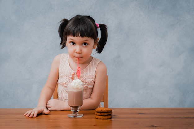 Small child girl drinks hot chocolate or cocoa with cookies through a cocktail tube.