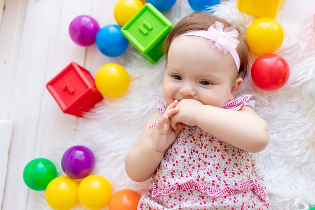 A small child girl lies in red clothes on a white Mat among toys balls and cubes