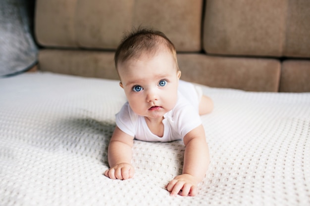 A small child a girl with blue eyes crawls on the bed