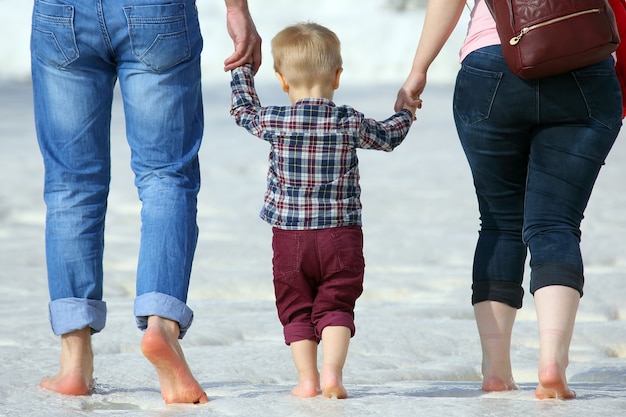 Small child goes barefoot on a wet surface holding hands of parents

