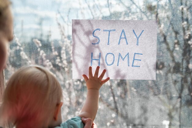 小さな子供は言葉で窓の紙のシートを保持しますSTAYHOME検疫隔離の概念