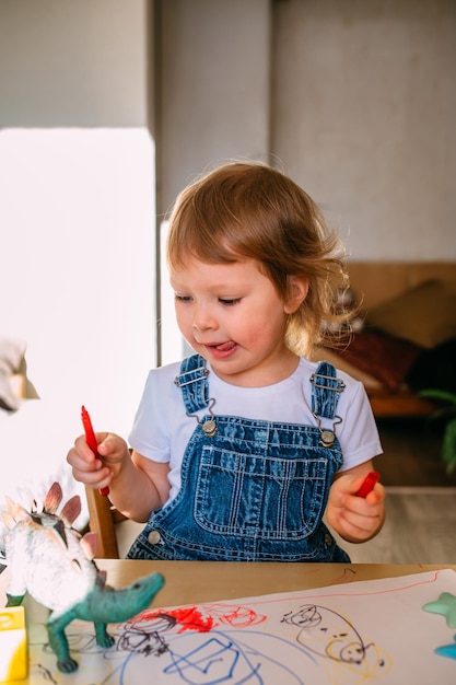 Маленький ребенок дома за детским столом рисует фломастерами