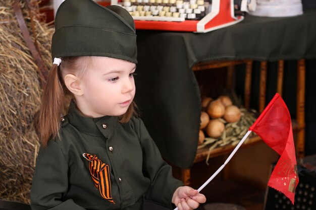 Фото Маленький ребенок в военной форме на празднике победы; украшения военного времени. стиль кантри. аккордеон; флаг. 9 мая