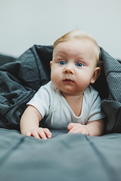 A small child is lying on a big bed at home Portrait of a fivemonthold baby lying on a gray bed Cheerful happy child