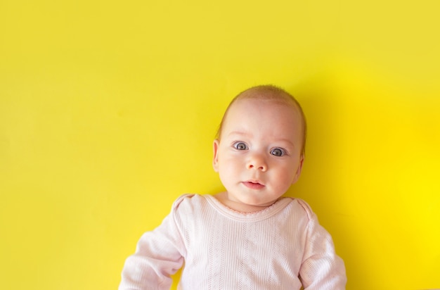 小さな子供が黄色い孤立した表面に仰向けに横たわっています。