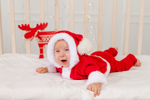 A small child is lying in a Santa costume in the crib and crying