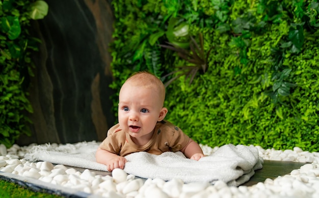 小さな子供が植物の壁のある緑の部屋で白い毛布の上に横たわっている